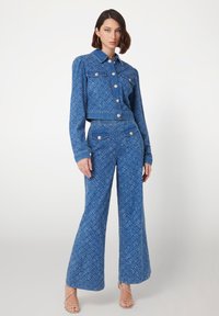 Jeans-set i två delar med en blåmönstrad kort jacka med guldknappar och vida byxor. Slät textur, avslappnad design.