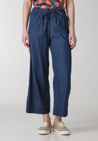 Pantaloni in denim blu scuro a gamba larga con cintura elastica e cordoncino. Presentano una forma dritta e un orlo rifinito. Indossati con sneakers casual.