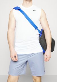 Camiseta blanca sin mangas deportiva, pantalones cortos azul claro, bolso negro con correa azul, que muestra un diseño sencillo y tela transpirable.