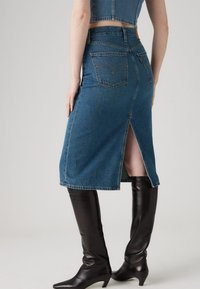 Blauwe denim midi-rok met een hoge split, voorzien van achterzakken en een klassiek vijfzakken ontwerp, in combinatie met knielange zwarte leren laarzen.