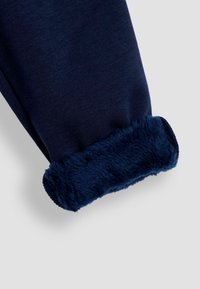 Meripihalla siniset sweatsuit-housut, joissa on pehmeä, pörröinen vuorikangas lahkeissa, ja sileä ulkopinta sekä kapeneva lahkeiden muoto.
