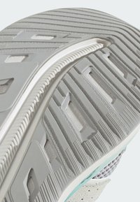 Potplat cipela s teksturiranom sivom gumom, koji sadrži uzorak i zakrivljeni bijeli naglasak duž rubova za poboljšano prianjanje.