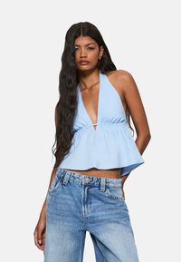 Top corto azzurro chiuso al collo con vita arricciata e orlo a campana, realizzato in un tessuto morbido, abbinato a jeans a vita alta in denim blu scolorito.