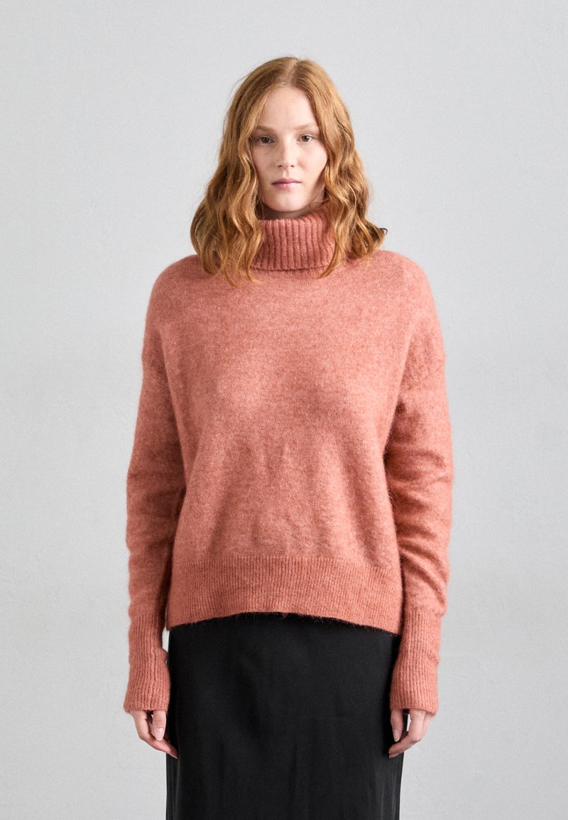 Light pink, loose-fitting sweater with a ribbed turtleneck, long sleeves, and a relaxed hem. Soft texture with a slightly fuzzy appearance.