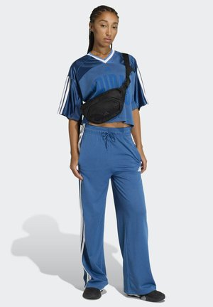 Completo atletico blu con maglia a rete larga e pantaloni abbinati con strisce laterali bianche. La borsa nera a tracolla completa l'outfit.