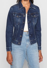 Jeansjacka i mörkblått, med knappstängning, två bröstfickor och kontrasterande sömmar. Matchad med ljusblå högmidjade jeans.