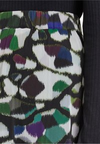 Printed skirt featuring a black background with abstract green, purple, and white shapes. Material is lightweight with a textured finish.