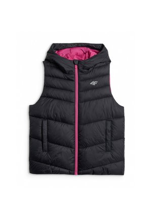 Jong meisje draagt een roze trainingspak en een zwart gewatteerd vest, staand tegen een effen grijze achtergrond.