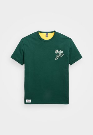 T-shirt en coton vert avec col intérieur jaune, présente un logo blanc "Polo" et un graphisme d'aile sur la poitrine gauche, ourlet droit, manches courtes.