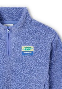 Pull polaire sherpa bleu lavande avec fermeture éclair quart de longueur et écusson sur la poitrine gauche portant l'inscription "La Maison AMV Super Vintage".