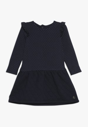 Mørkeblå kjole med lange ærmer, prikket mønster på toppen, flæseaccent på skuldrene og quiltet tekstur på skørtet. Gulddetalje med logo.