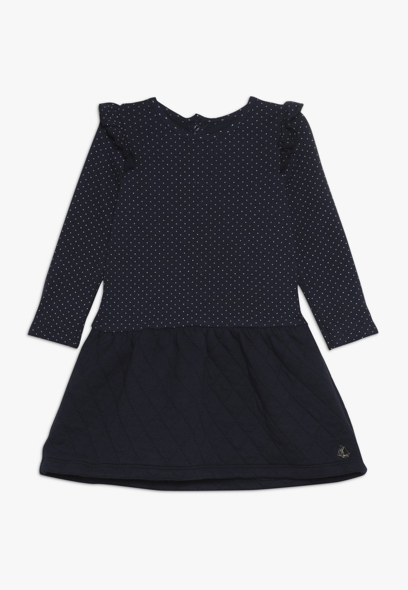 Robe bleu marine à manches longues, motif à pois sur le haut, accent volants sur les épaules, et texture matelassée sur la jupe. Détail logo doré.