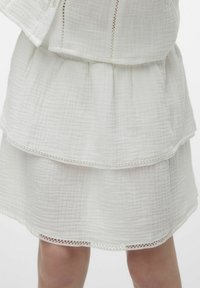 Falda blanca de capas hecha de un tejido texturizado, con un diseño de volantes y un delicado bordado en el dobladillo.