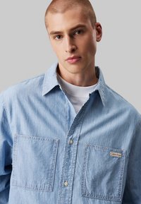 Hele sinine denim särk pikade varrukatega, nööbid allavajutatud kraega, kahe rinnataskuga ja Calvin Kleini logo lapiga vasakus taskus. Struktuurne kangas.