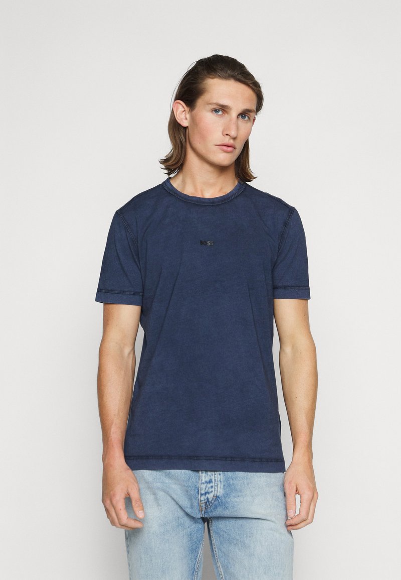 Ναυτικό μπλε κυκλικό t-shirt από βαμβάκι, με κοντά μανίκια και μια διακριτική μαύρη λογότυπο "BOSS" στο στήθος. Φοριέται με ανοιχτόχρωμο μπλε τζιν.