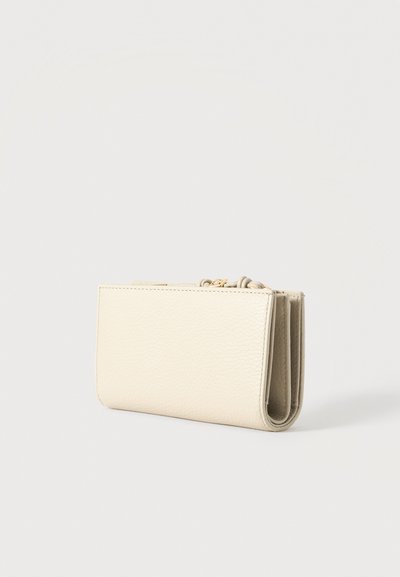 Pequeña cartera de cuero texturizado color crema con bordes cosidos y una cremallera dorada visible sobre un fondo blanco.