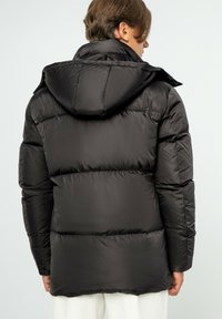 Giacca a vento nera con cappuccio, caratterizzata da sezioni imbottite e una finitura liscia e lucida. Il design include un colletto rialzato e una tasca a pattina.