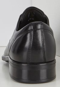 Scarpa in pelle nera con una finitura liscia, punta rotonda e tacco basso e massiccio. Caratterizzata da dettagli di cucitura lungo i lati.