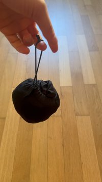 Mano sosteniendo una pequeña bolsa negra con cordón y cierre, fondo de suelo de madera.