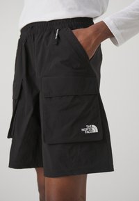 Svarta cargoshorts i lättviktig tyg, med elastisk midja, flera stora fickor och en vit logotyp på nedre vänstra sidan.