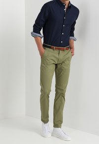 Laivastonsininen napillinen paita ruudullisilla kalvosimilla, oliivinvihreät housut, ruskea vyö ja valkoiset tennarit. Slim fit -leikkaus, sileä kangas ja rento muotoilu.