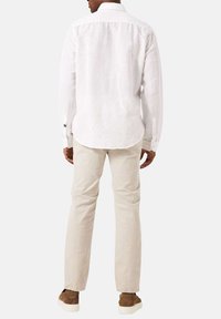 Witte linnen blouse met lange mouwen, een achterpand met schouderpas, knoopmanchetten en beige slim-fit broek. Bruine suède sneakers maken de outfit compleet.