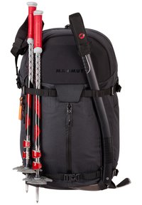 Czarny plecak z logo Mammut; ma czerwone kijki trekkingowe i czekan. Materiał jest teksturowany, z pewnymi paskami i zamkami błyskawicznymi.