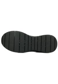 Suola di scarpa in gomma nera con un design testurizzato. Presenta scanalature profonde per una maggiore aderenza e il logo "GUESS" in rilievo nella zona del tallone.