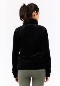 Schwarze Fleecejacke mit hohem Kragen und langen Ärmeln. Weicher Stoff, figurbetonter Schnitt und keine sichtbaren Beschläge oder Verzierungen.