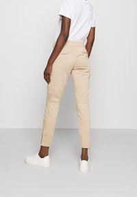 Beige cargo kalhoty s elastickým pasem, slim fit, bočními kapsami a zadními kapsami na patku, v kombinaci s bílými teniskami a bílou košilí.