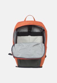 Sac à dos orange et vert avec un intérieur spacieux gris, des sangles ajustables et des bandes élastiques noires pour sécuriser les objets à l'intérieur.