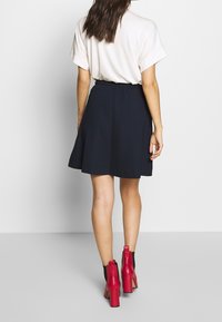 Svart utsvängd kjol med elastisk midjeresår, kombinerad med en vit lös t-shirt och röda grova högklackade ankelboots.