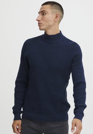 Suéter pullover de color azul marino con textura de waffle, cuello alto, puños y dobladillo de canalé, y una silueta ajustada.