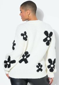 Übergroßer weißer Strickpullover mit schwarzen Blumenmustern, gerippten Bündchen und Kragen. Weiche Textur mit lockerem Schnitt, für Komfort entworfen.