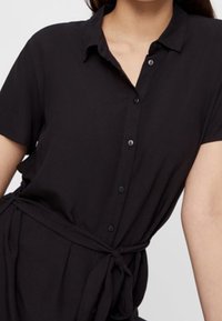 Black short-sleeve dress with a button-up front, collar, and waist tie. Made from lightweight fabric with a smooth texture.