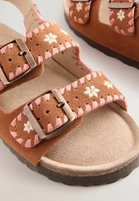 Braune Wildleder-Sandalen mit rosa Nähten und Blumenstickerei. Verfügt über zwei verstellbare Schnallen und ein strukturiertes, gepolstertes Fußbett.