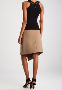 Sort ærmeløs top med lynlås og gennemsigtige stropper, kombineret med et tan asymmetrisk nederdel. Sorte hæle med stropper fuldender outfittet.