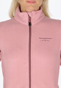 Giacca in fleece rosa con colletto alto, chiusura a zip e logo stampato. Texture morbida e design aderente, adatto per essere indossato a strati.