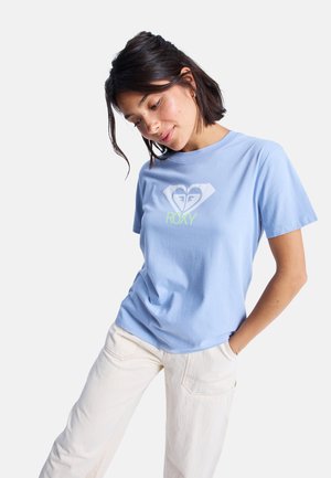 T-shirt en coton bleu clair avec col rond et manches courtes, présentant un logo en forme de cœur blanc et vert néon avec le texte "ROXY" au centre.
