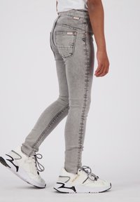 Jeans ajustados grises con un lavado desgastado, bolsillos delanteros y traseros, y herrajes de color cobre, combinados con zapatillas blancas con acentos negros.
