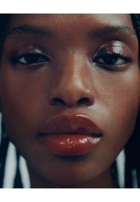 Lähikuva kasvoista, joissa sileä, tumma iho. Kiiltävät, syvän punaiset huulet ja neutraali silmämeikki, jossa korostetut ripset. Terve ja hehkuva iho.