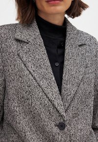 Textured black and white striped blazer with a notched collar, single button closure, and pockets, layered over a black top.