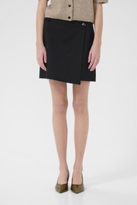 Black wrap skirt with an asymmetrical hem, featuring a side button closure. Material appears smooth; paired with pointed-toe green heels.