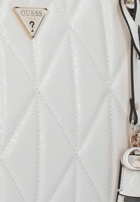 Bolso blanco acolchado con patrón de logo en relieve, herrajes plateados, emblema triangular de la marca y un charm desmontable en una correa negra.