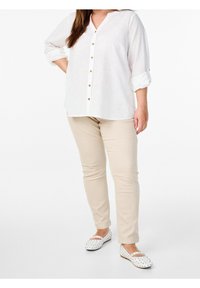 Weiße, knopf-Down-Bluse mit V-Ausschnitt und hochgeschlagenen Ärmeln, kombiniert mit beigen Slim-Fit-Hosen und weißen Slippern mit einem Punkte-Muster.