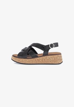 Black leather wedge sandal with crisscross straps, cork-textured midsole, and circular metal buckle on adjustable strap.