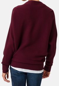 Suéter burdeos de punto acanalado con un corte holgado, mangas largas y un escote redondeado, combinado con una camisa blanca por debajo.