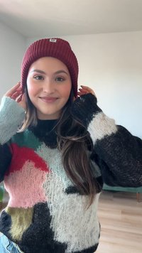 Bordová pletená čepice s ribovanou strukturou a nášivkou loga, v kombinaci s vícebarevným silným svetrem s odvážnými vzory a různými texturami.