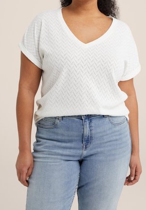 Biały top z krótkim rękawem i dekoltem w serek z teksturowanym wzorem jodełki, w połączeniu z jasnoniebieskimi, wysokim stanem dżinsami.