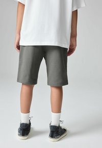 Grå bomullsshorts med en slät yta, med fållen som når till mitten av låret, kombinerat med vita ribbade strumpor och mörka högknäppta sneakers.